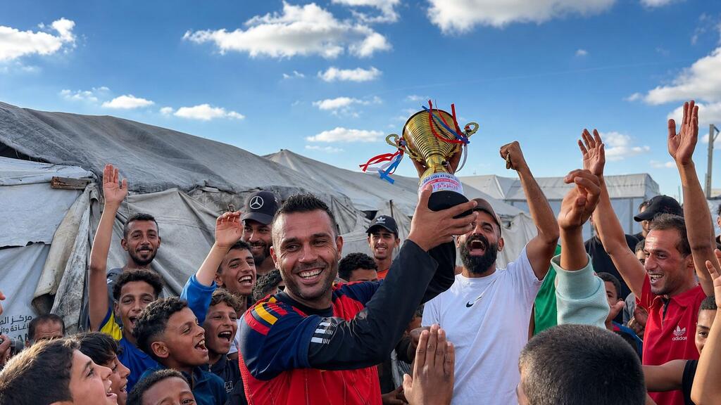لاعب كرة القدم الفلسطيني أسعد العزابي يحمل كأس بطولة مخيمات نازحي رفح، يحتفل مع حشد من الشباب والأطفال في مواصي خان يونس.